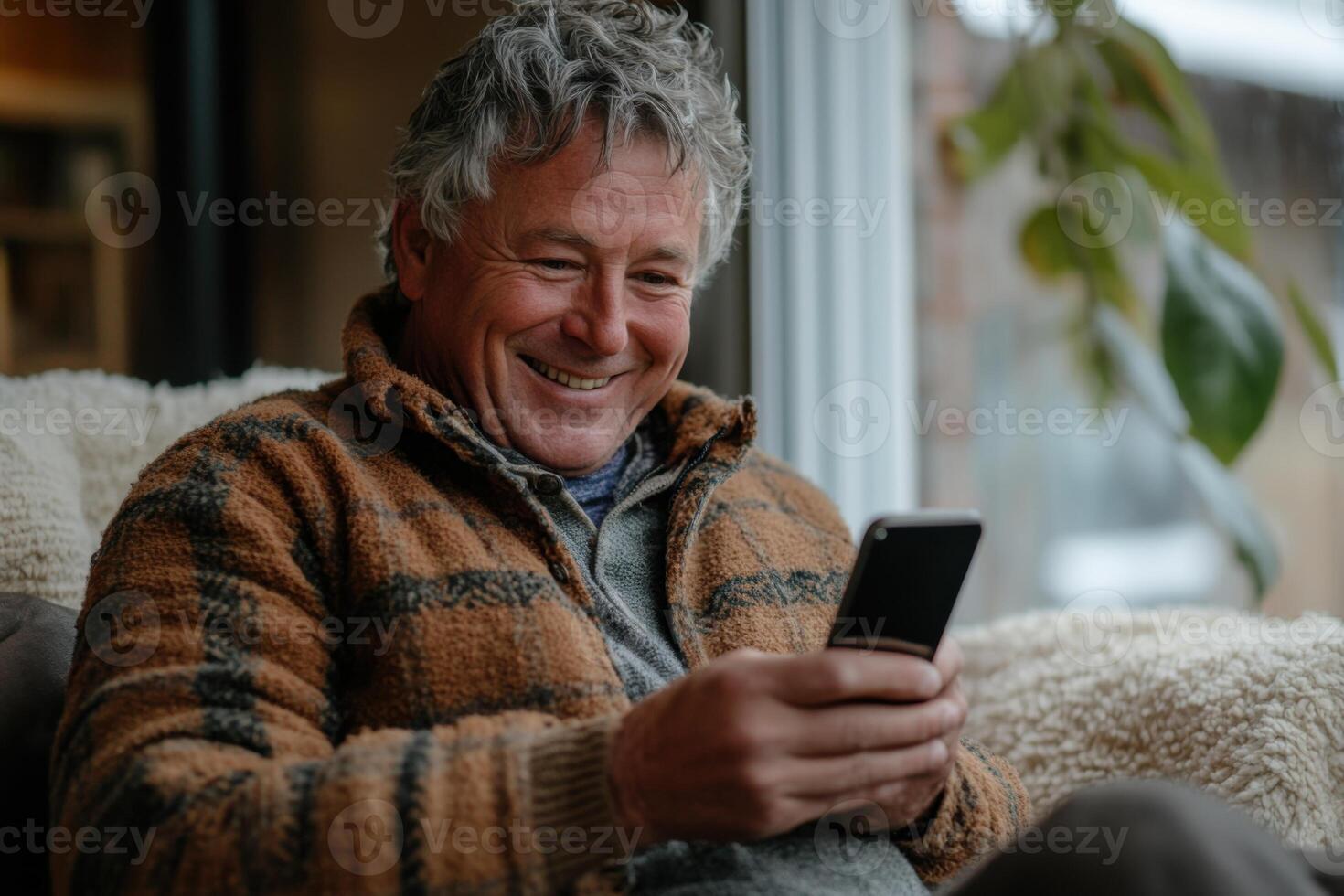 Man sitting relaxing at home. Person is smiling while looking at the screen of a mobile phone device. Indoor scene with natural light. photo