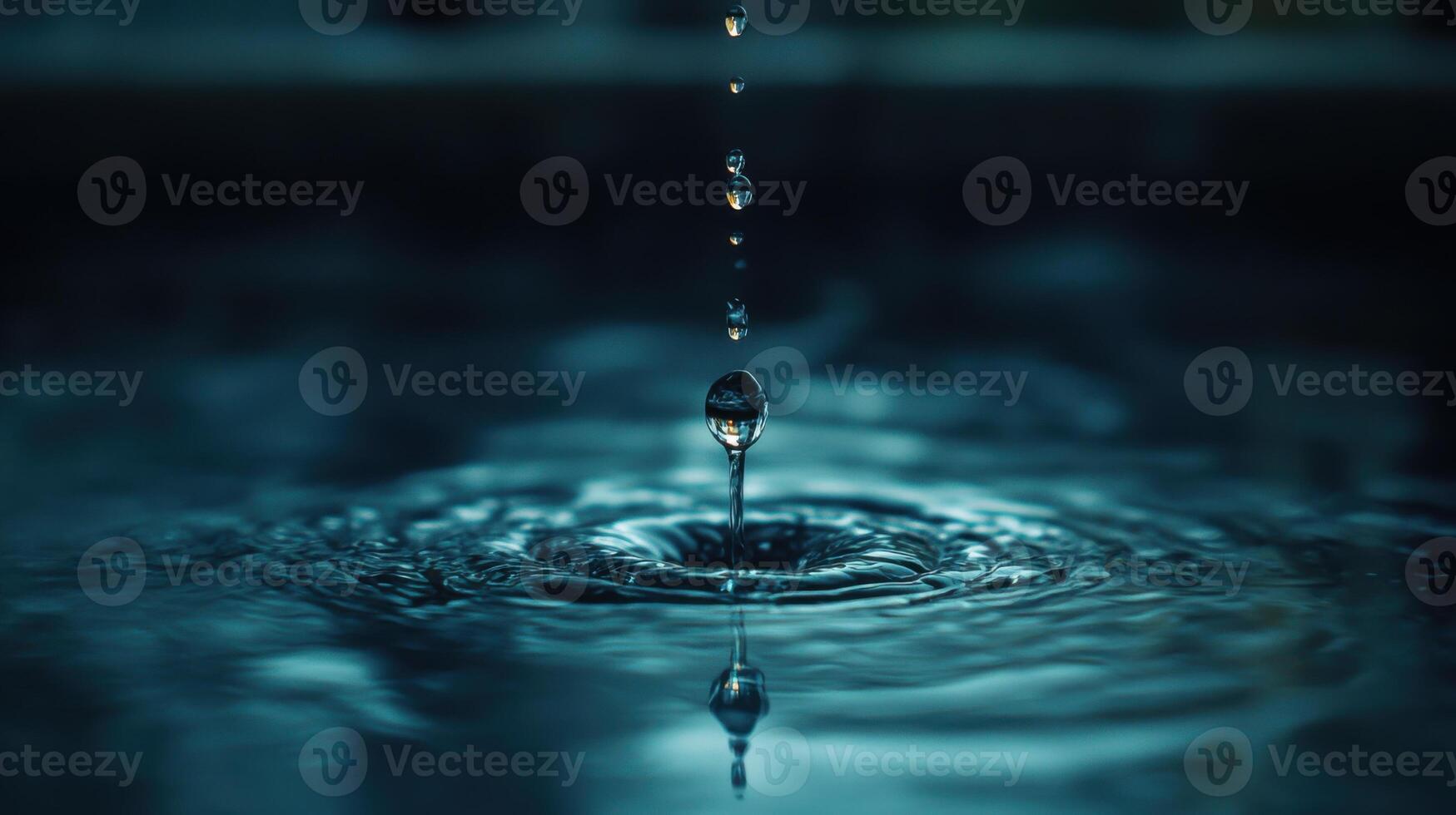 Water drop falls into water. Ripple effect is visible. Surface tension creates a clear reflection. Drops form on their way down. Water is blue. photo