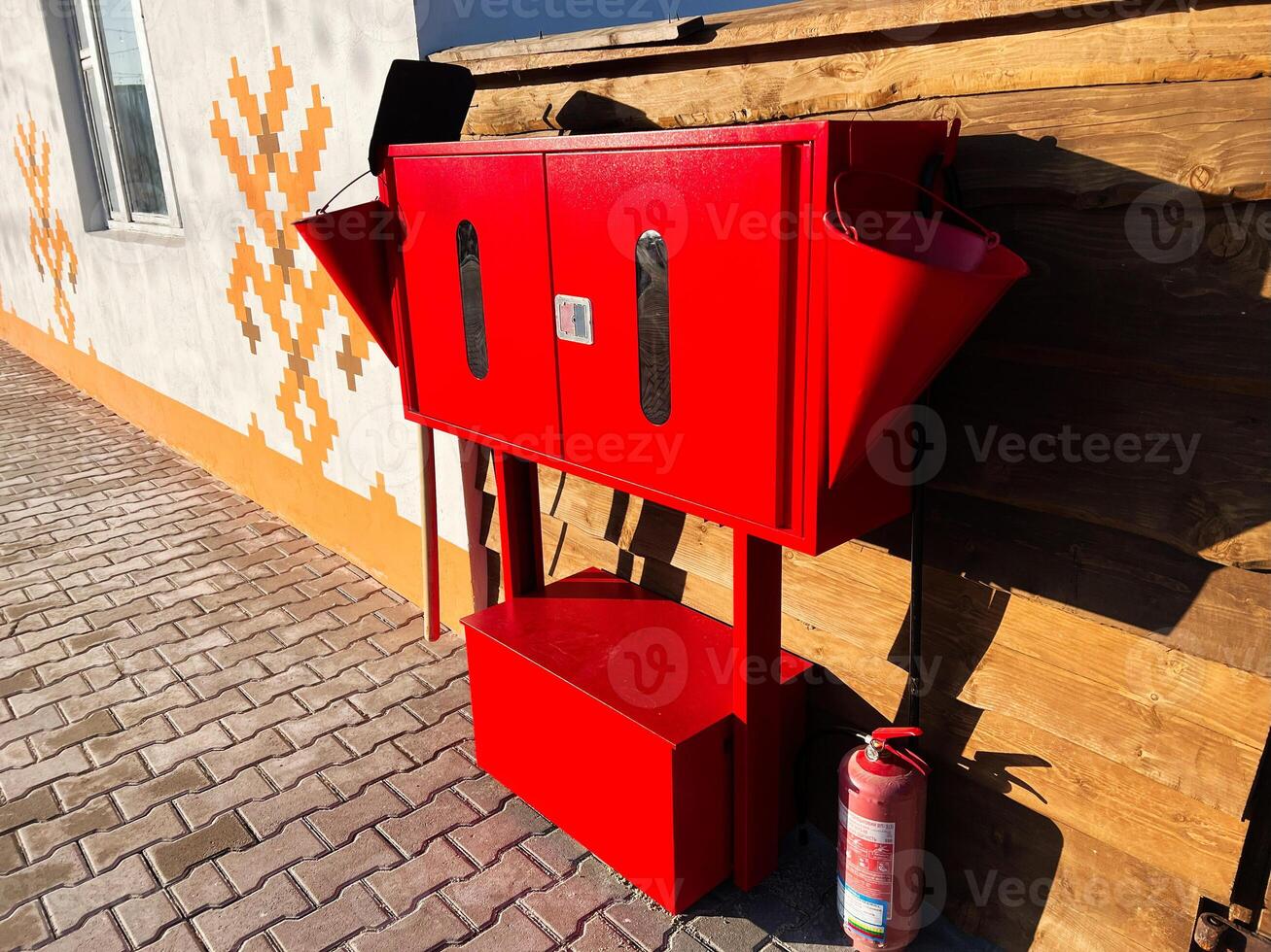 Red firefighting equipment with extinguisher and bucket on brick patio photo