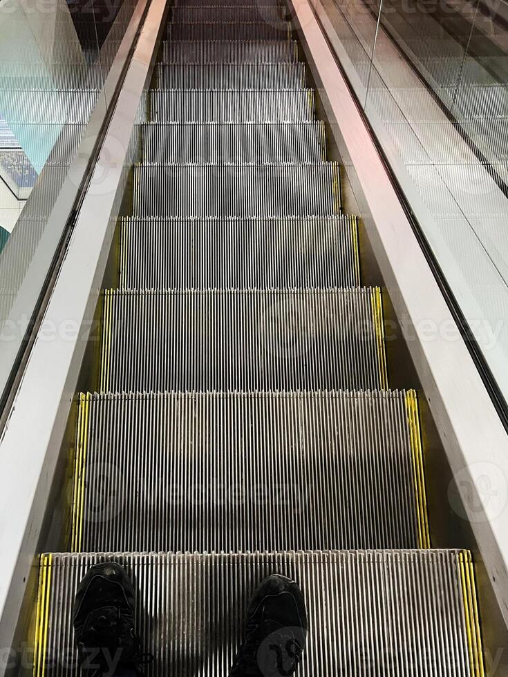 View looking down at metal escalator steps with reflective sides in urban setting photo