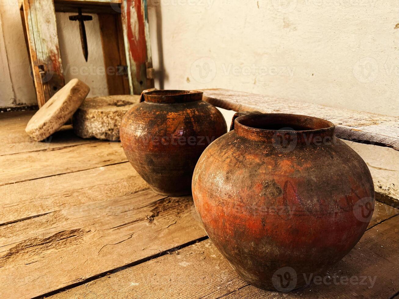 Rustic clay pots and milling tools in a historic wooden interior setting photo