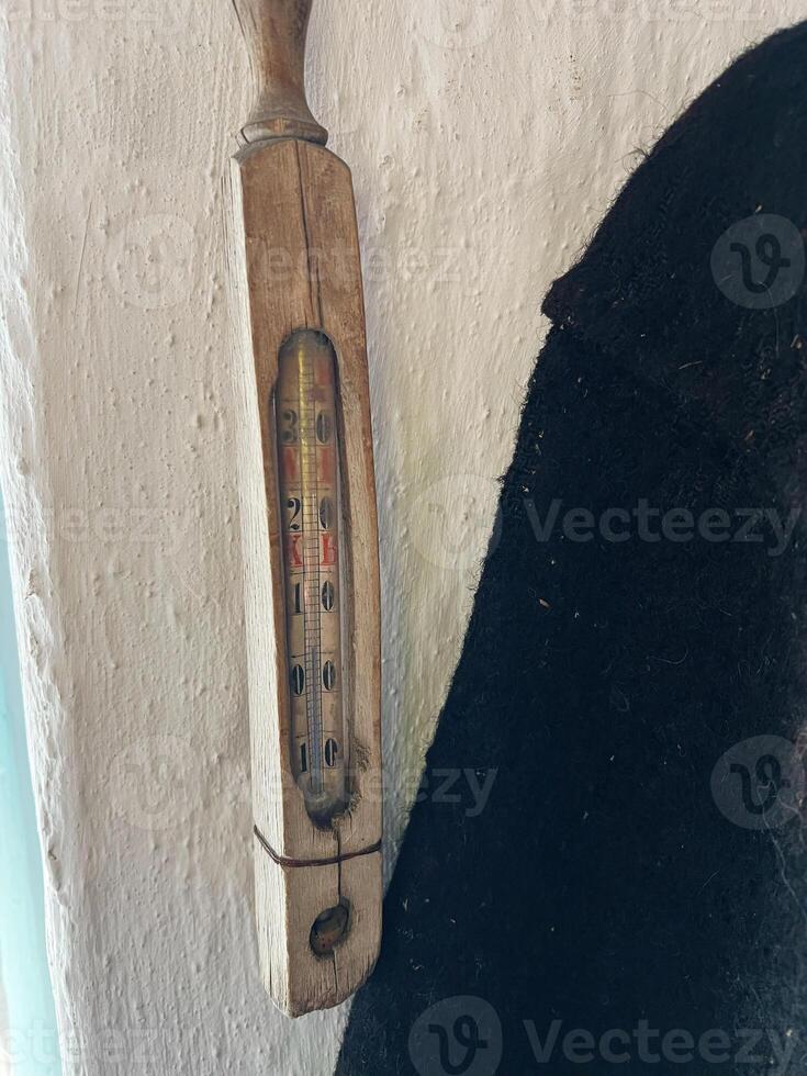 Vintage wooden thermometer mounted on a rustic wall with visible texture photo