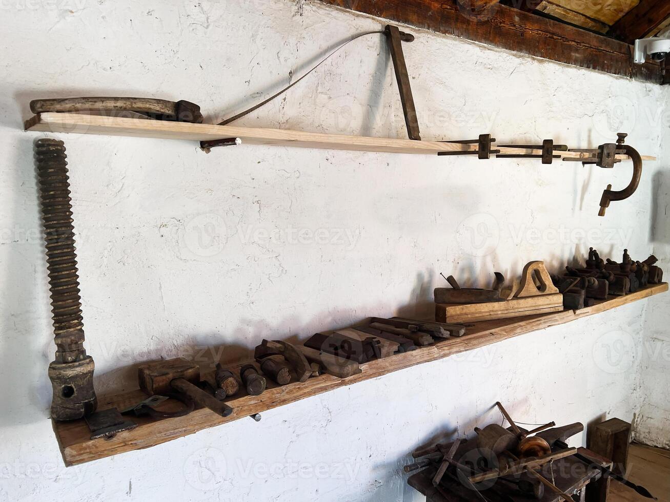 Rustic workshop tools displayed on wooden shelves against a white plastered wall photo