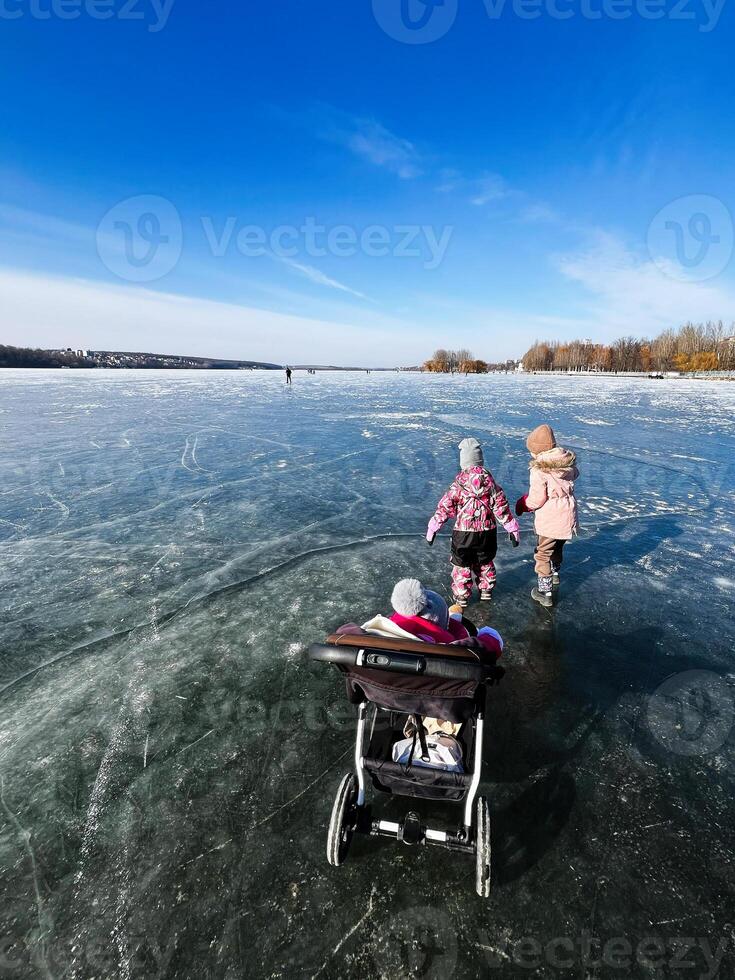 Family enjoying a winter walk on a frozen lake under a clear blue sky photo