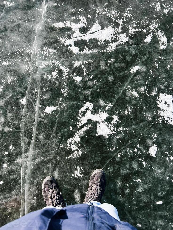 Person standing on a natural frozen lake with visible ice cracks and snow photo