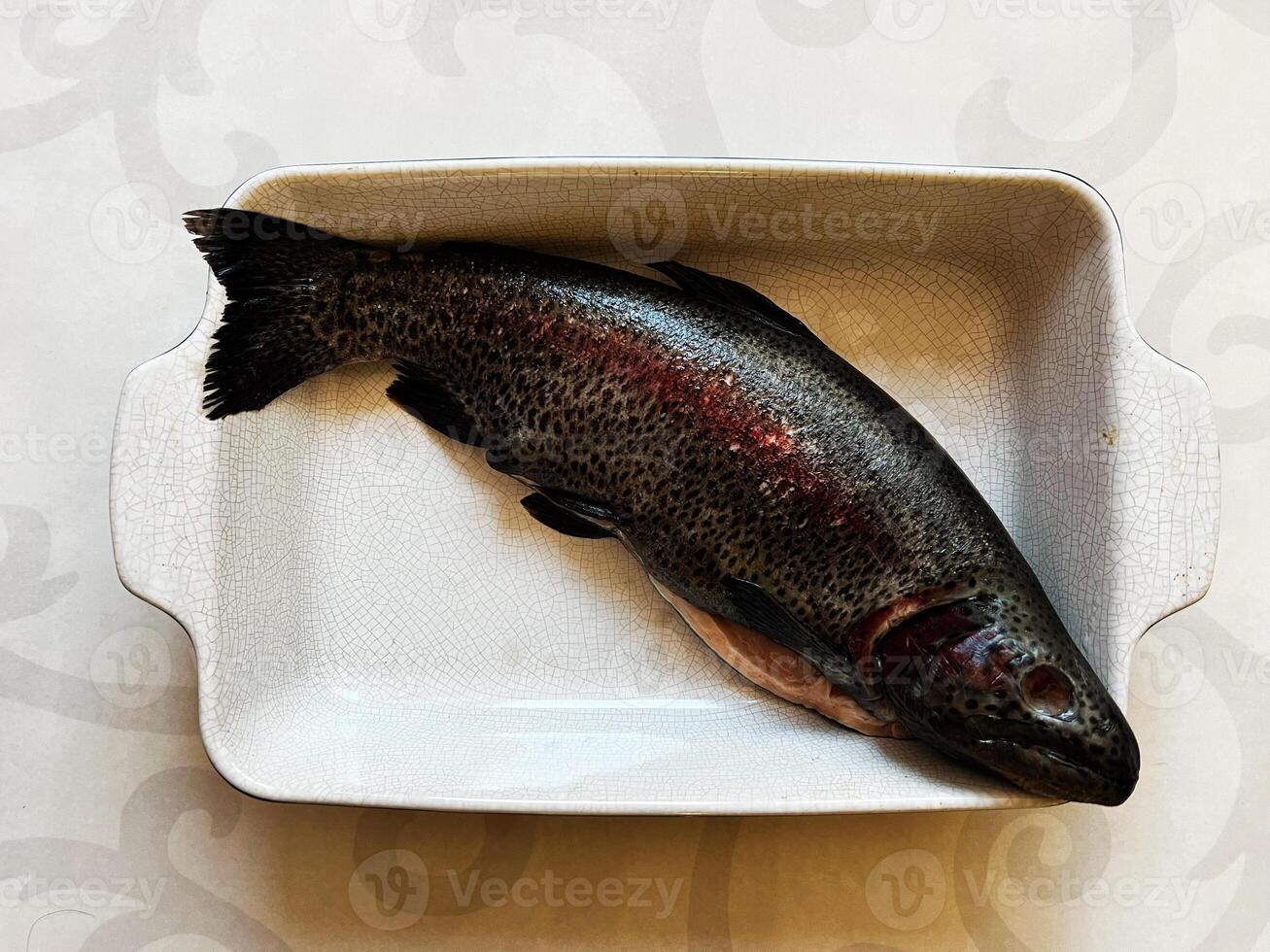Fresh rainbow trout in a white baking dish on a light patterned surface photo