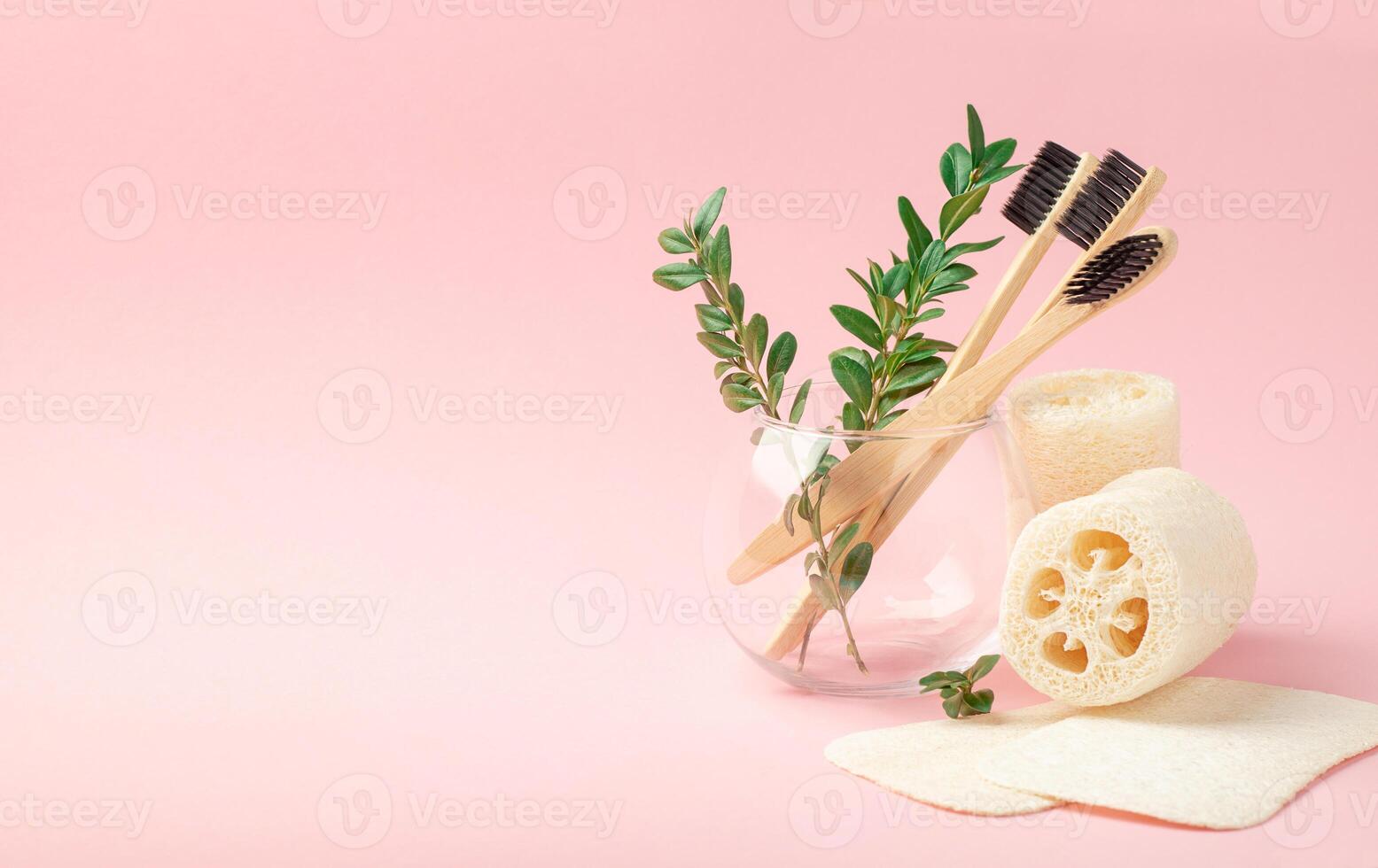Three bamboo, wooden brushes in a glass cup on a pink background. Loofah washcloths photo