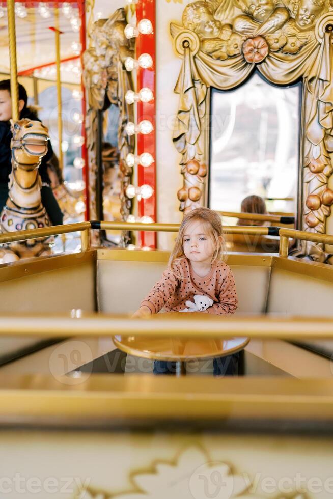 Little girl sits at a table on a carousel at a fair and looks into the distance photo