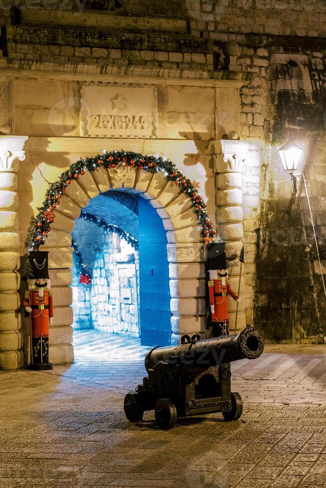 Old cannon stands near the arched entrance to an old building with figurines of soldiers on the sides photo