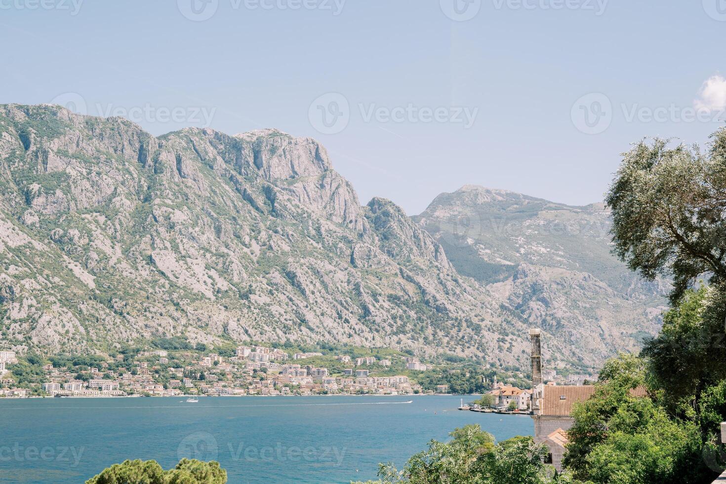 View over green tree branches and red roofs of houses on the sea with mountains in the background photo