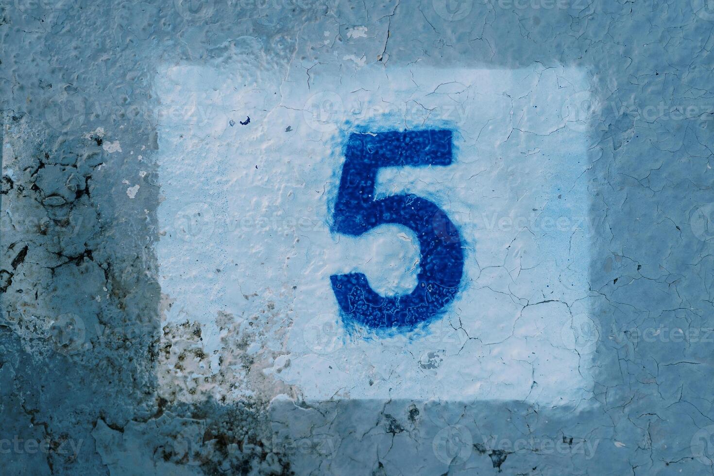Number five painted on a blue mud-stained wall in a white rectangle photo