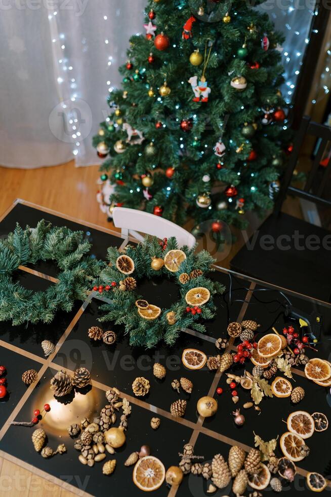 Accessories for the New Year wreath lie on the table near the decorated Christmas tree photo