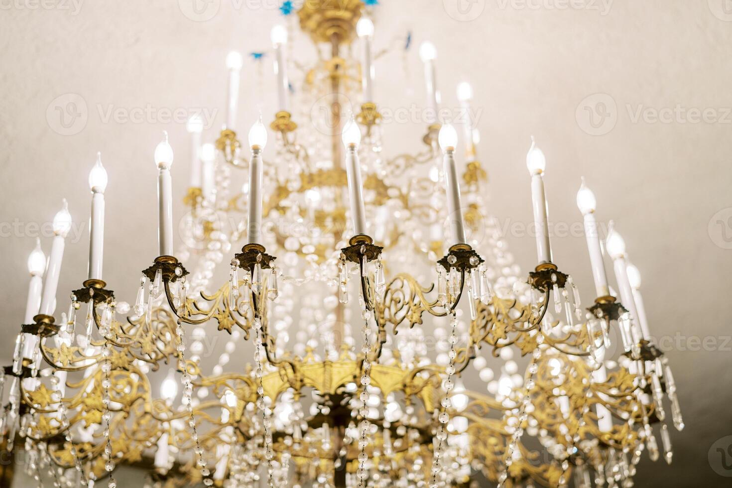 Antique chandelier with crystal pendants and candle lamps hangs from the ceiling photo