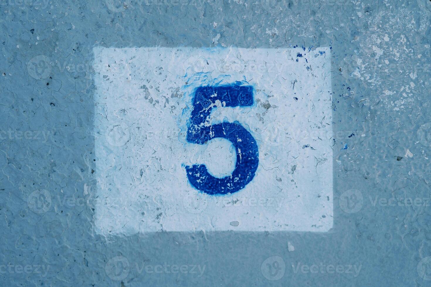 Number five with scratched paint drawn on a blue wall in a rectangle photo