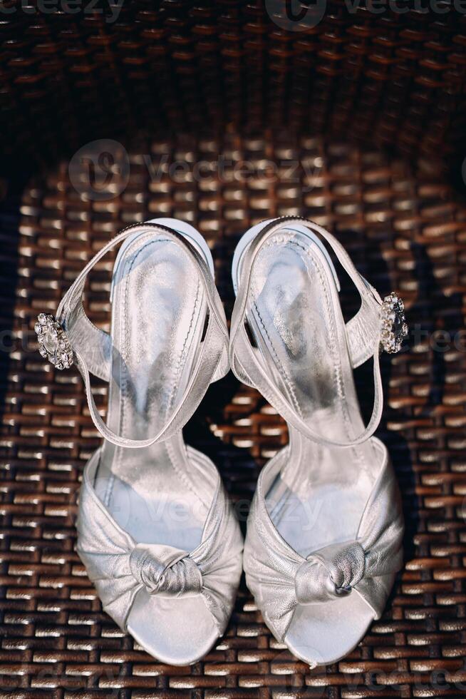 Bride silver shoes with buckles stand on a brown wicker chair photo