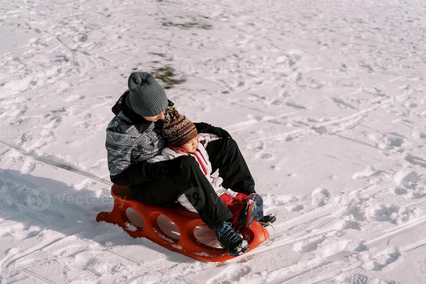 Mom with a small child are sitting on a sleigh on a snowy plain photo