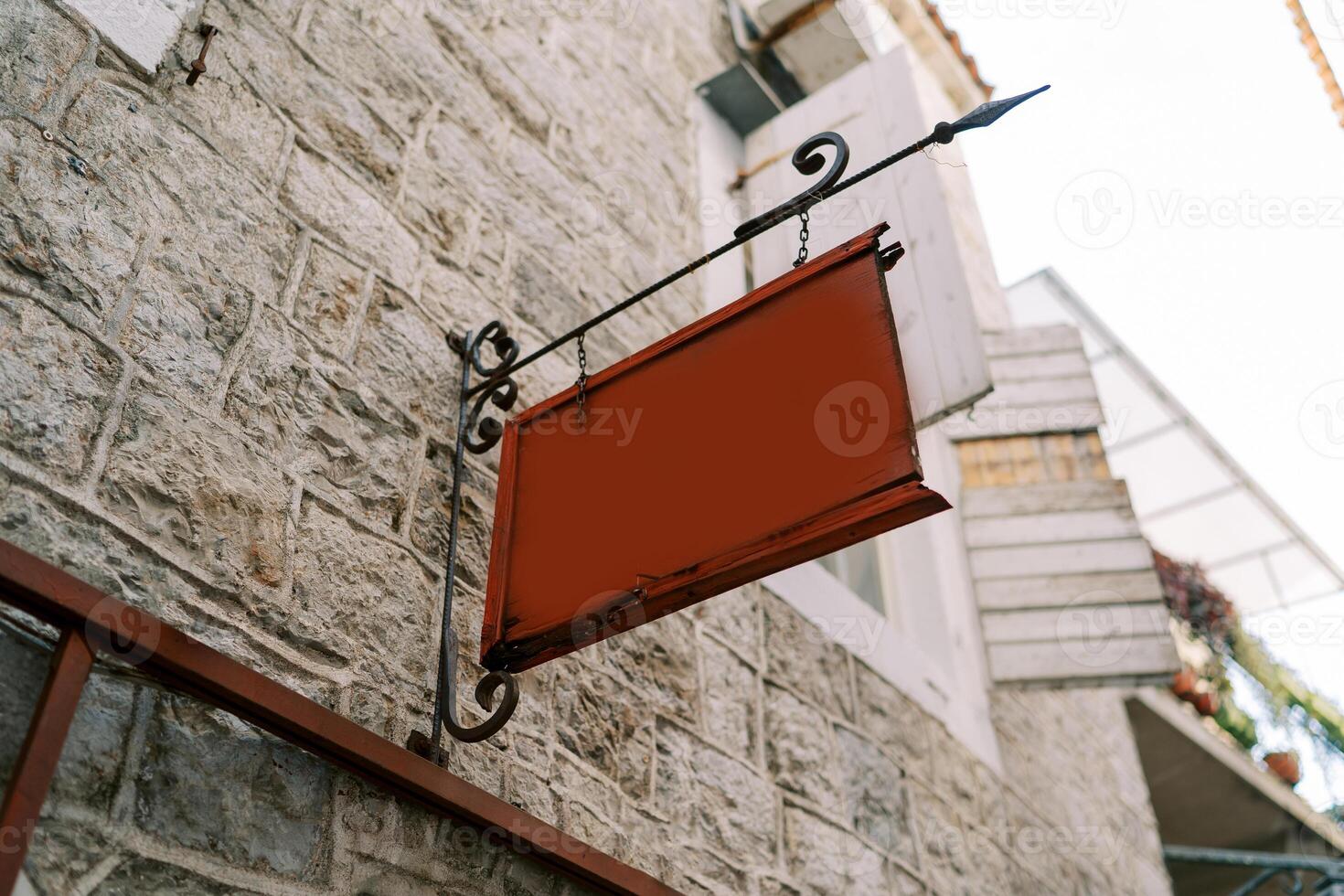 Empty tablet hangs on a forged signpost on the stone facade of an old house photo
