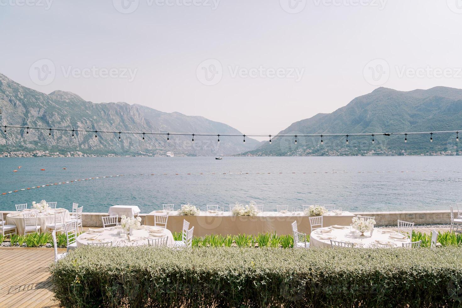 Festive served tables stand on a wooden terrace near the fence above the sea with a view of the mountains photo