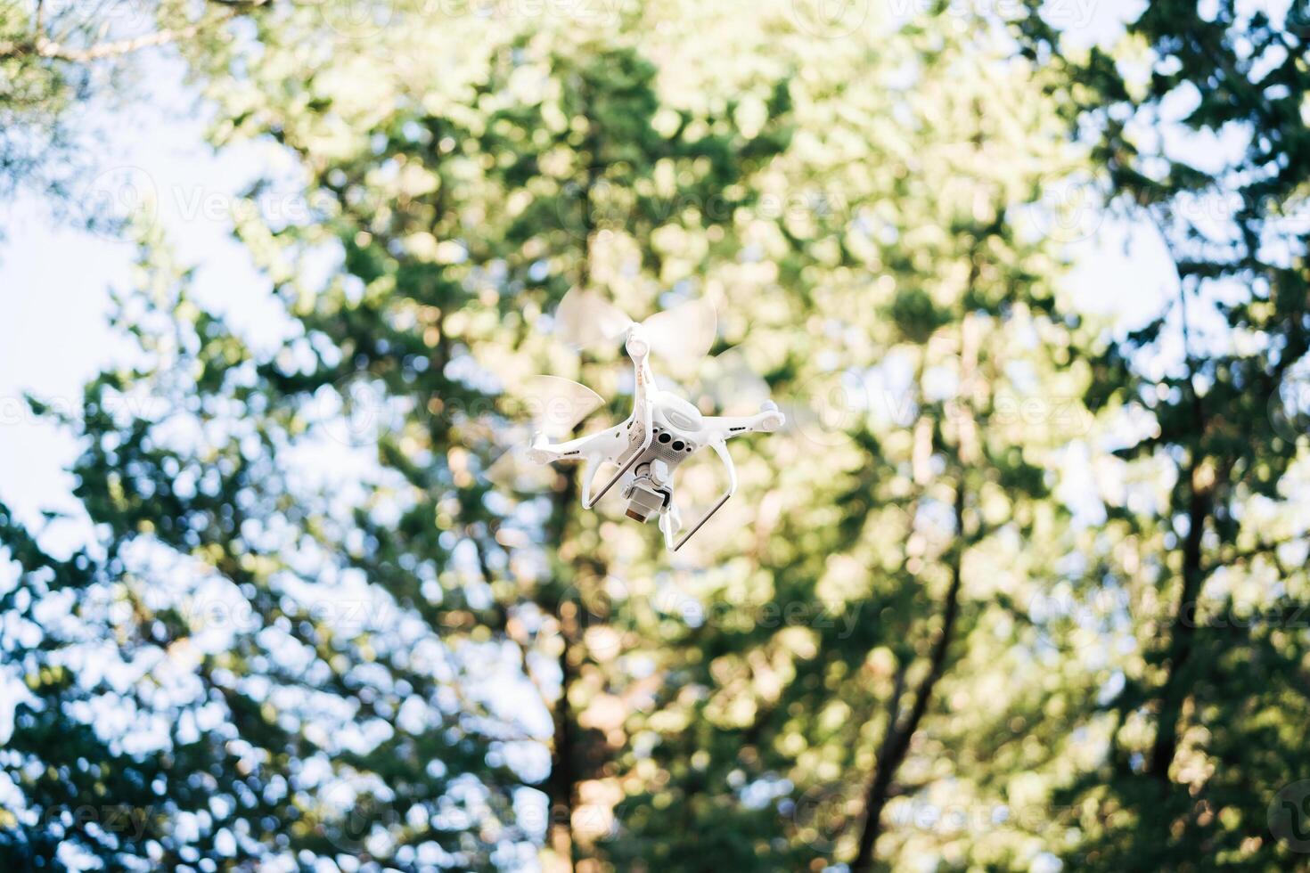 White quadcopter soars in the air against the background of trees in the park photo
