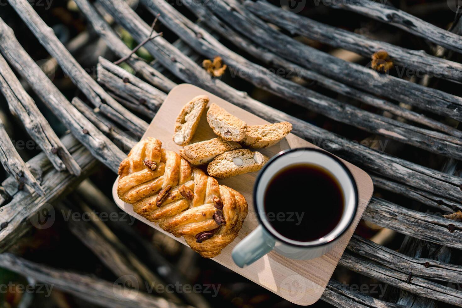 Coffee in a mug stands on a wooden board next to a bun and crackers in the park photo
