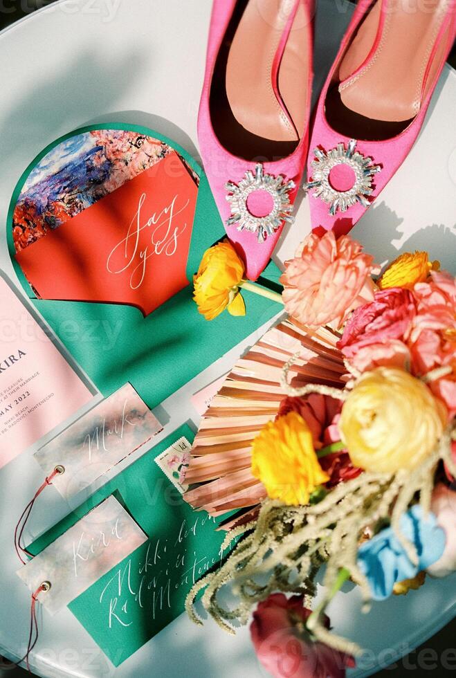 Bride pink shoes stand on the table next to colorful invitations and a bright bouquet of flowers photo