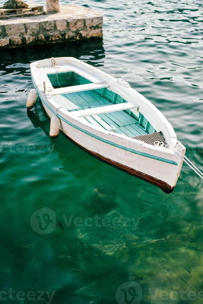 White fishing boat with a green bottom is moored at a stone pier photo