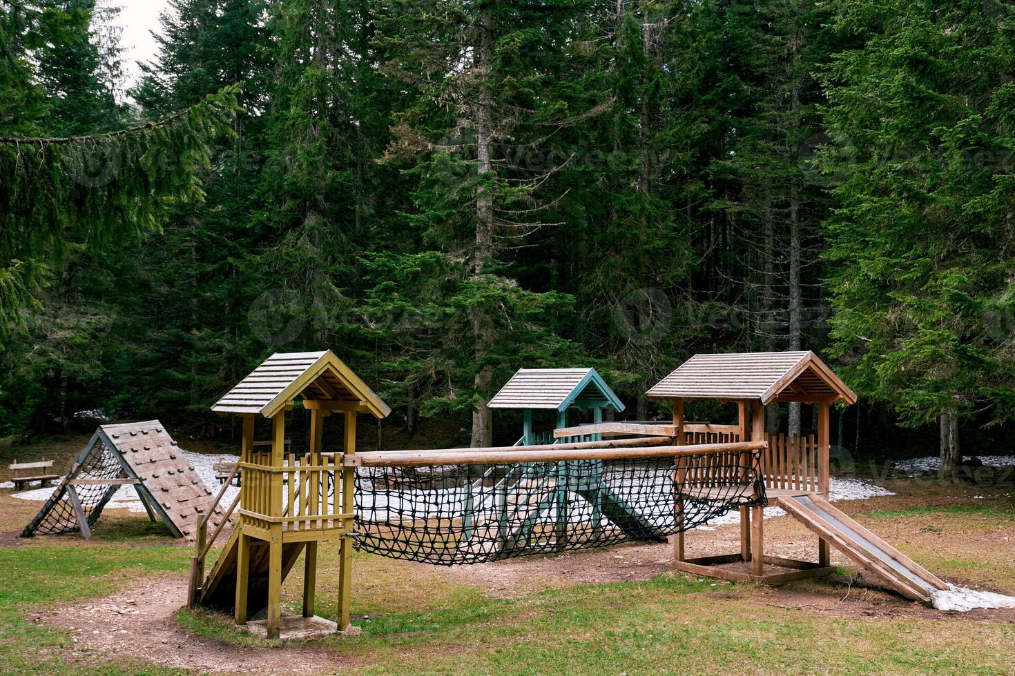 Wooden playground with an obstacle course and a climbing wall in a green forest photo