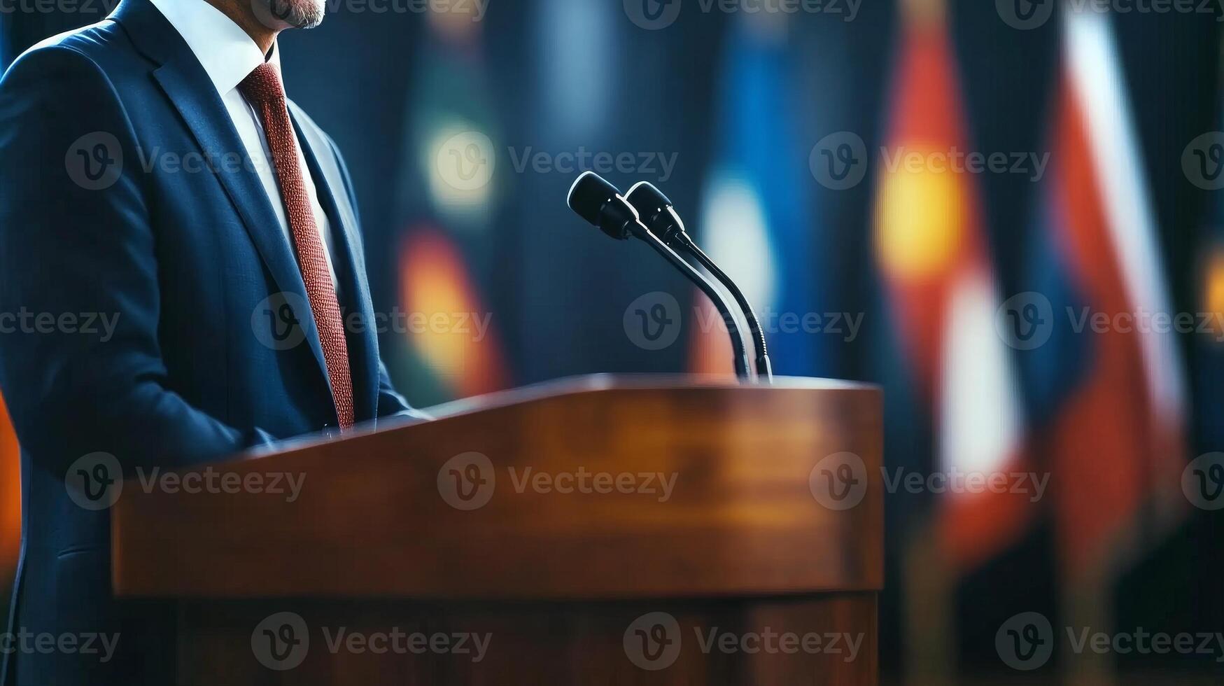 A speaker stands confidently at a podium during an international conference, with colorful flags representing various nations displayed behind. photo