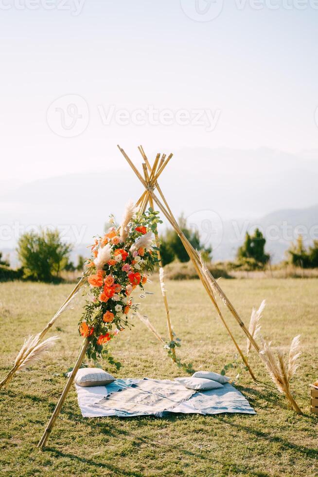 Boho-style wedding arch stands on a green lawn above a bedspread with pillows photo