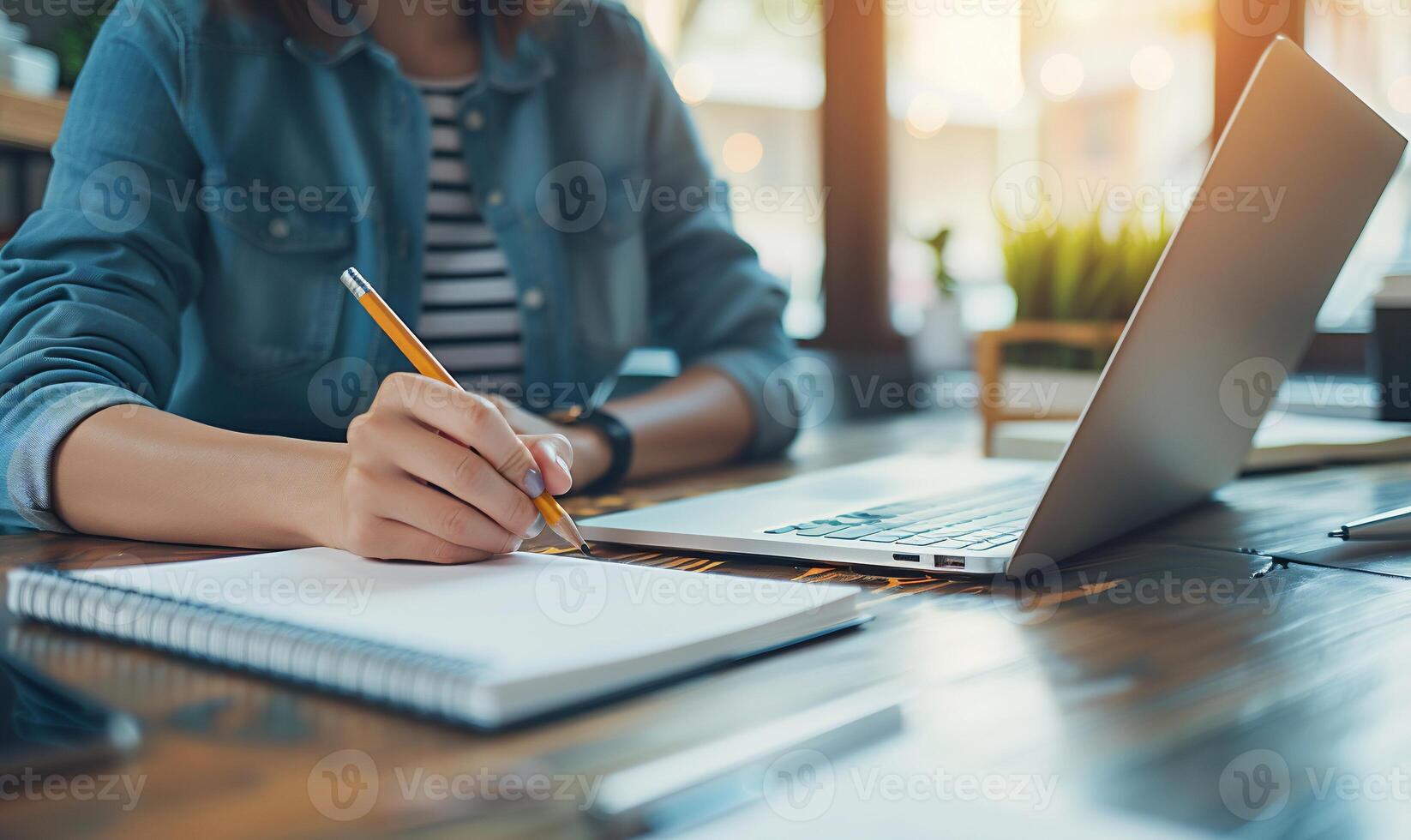 A woman writing on a notebook while sitting at a desk with a laptop photo