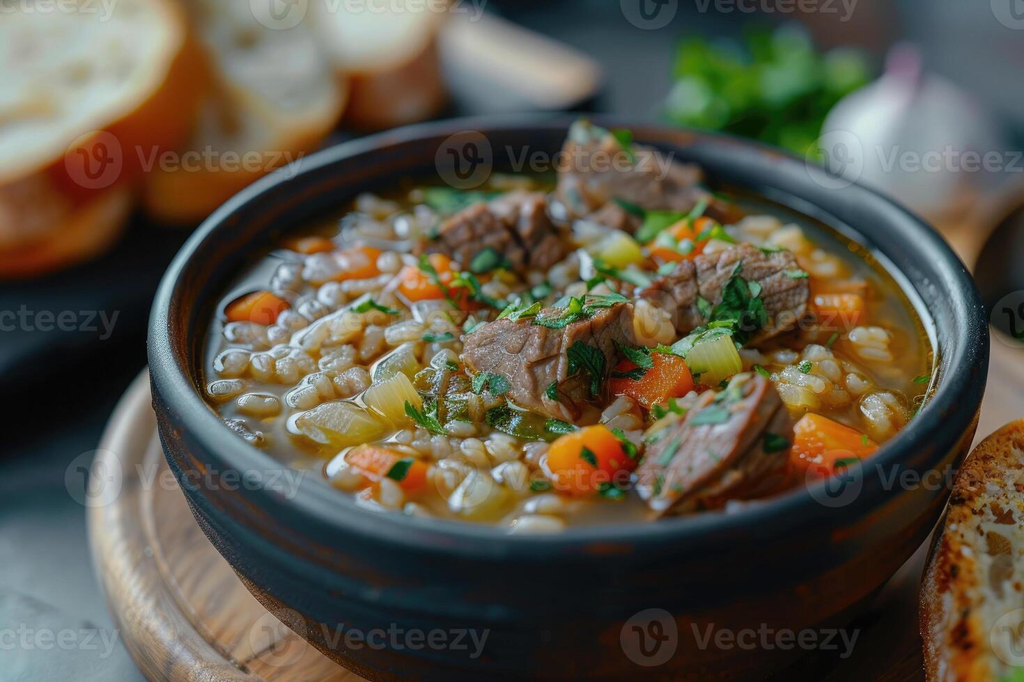 A hearty bowl of beef soup with vegetables and barley, served with bread photo