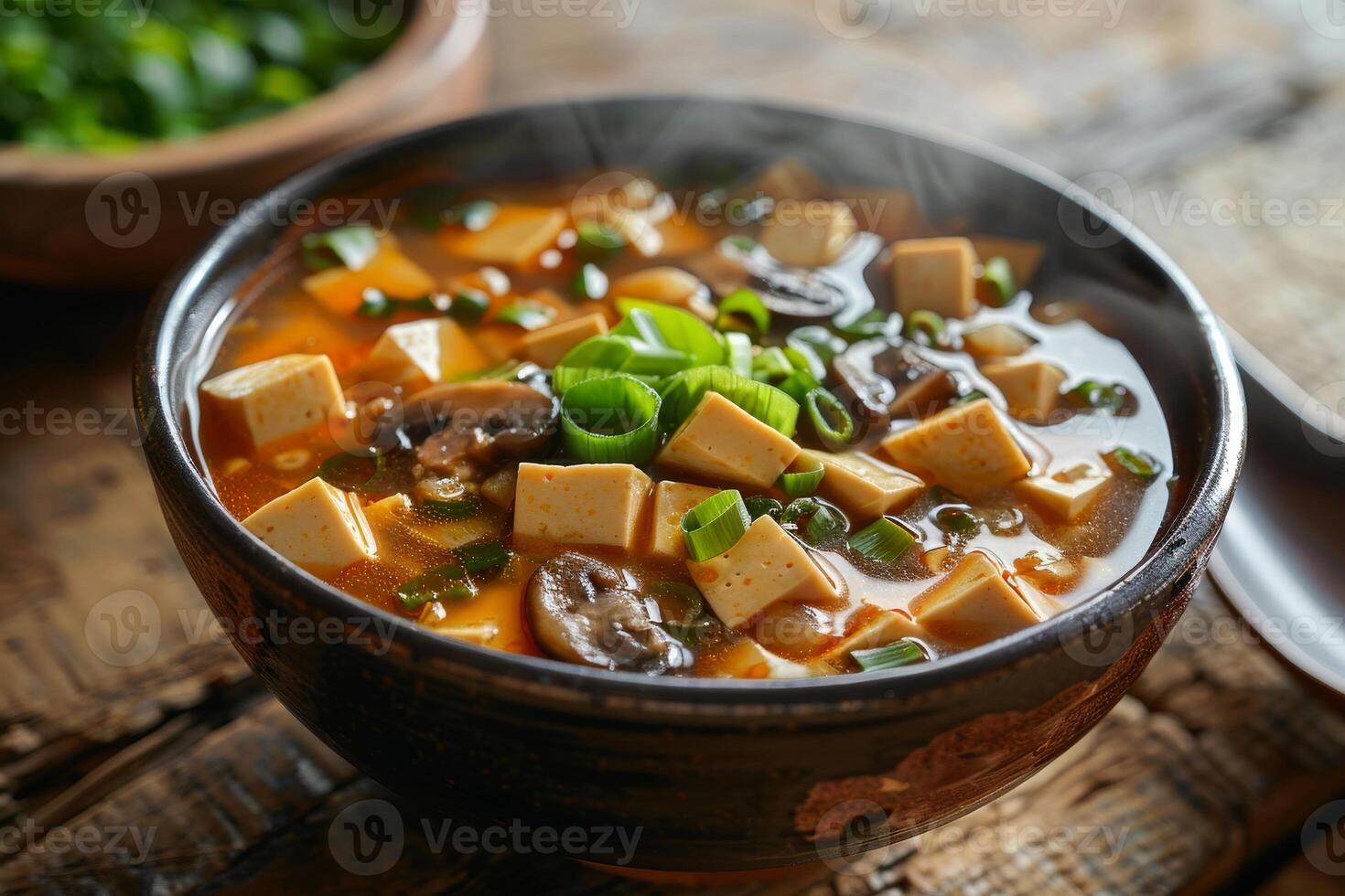 A steaming bowl of spicy tofu soup with mushrooms and green onions photo