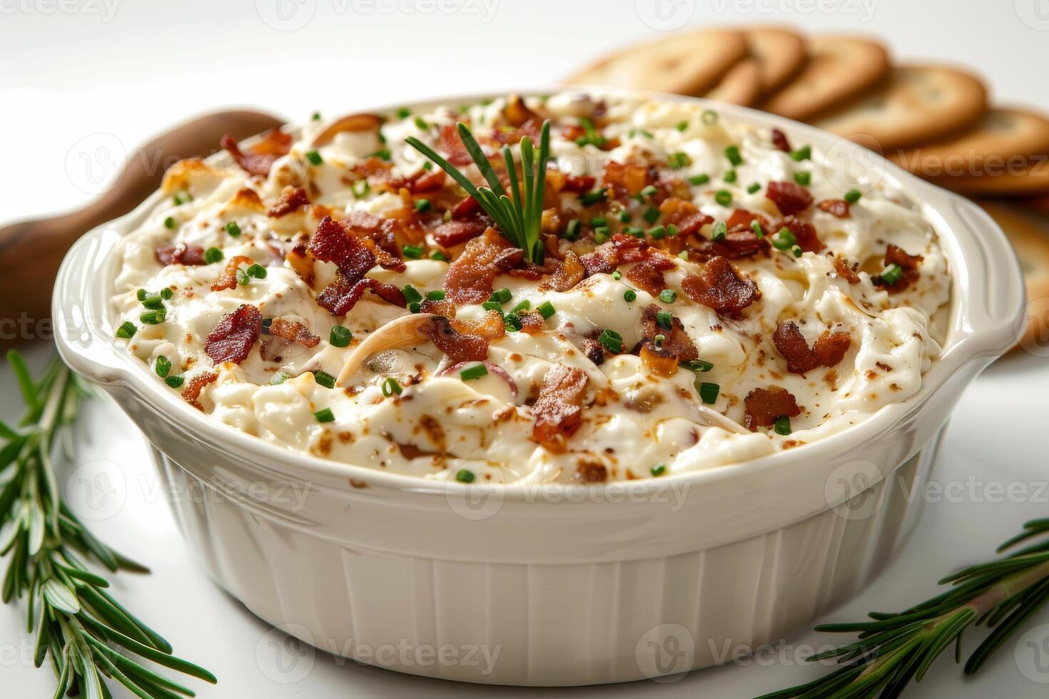 Creamy dish topped with bacon and herbs, served in a white bowl with snacks nearby. photo