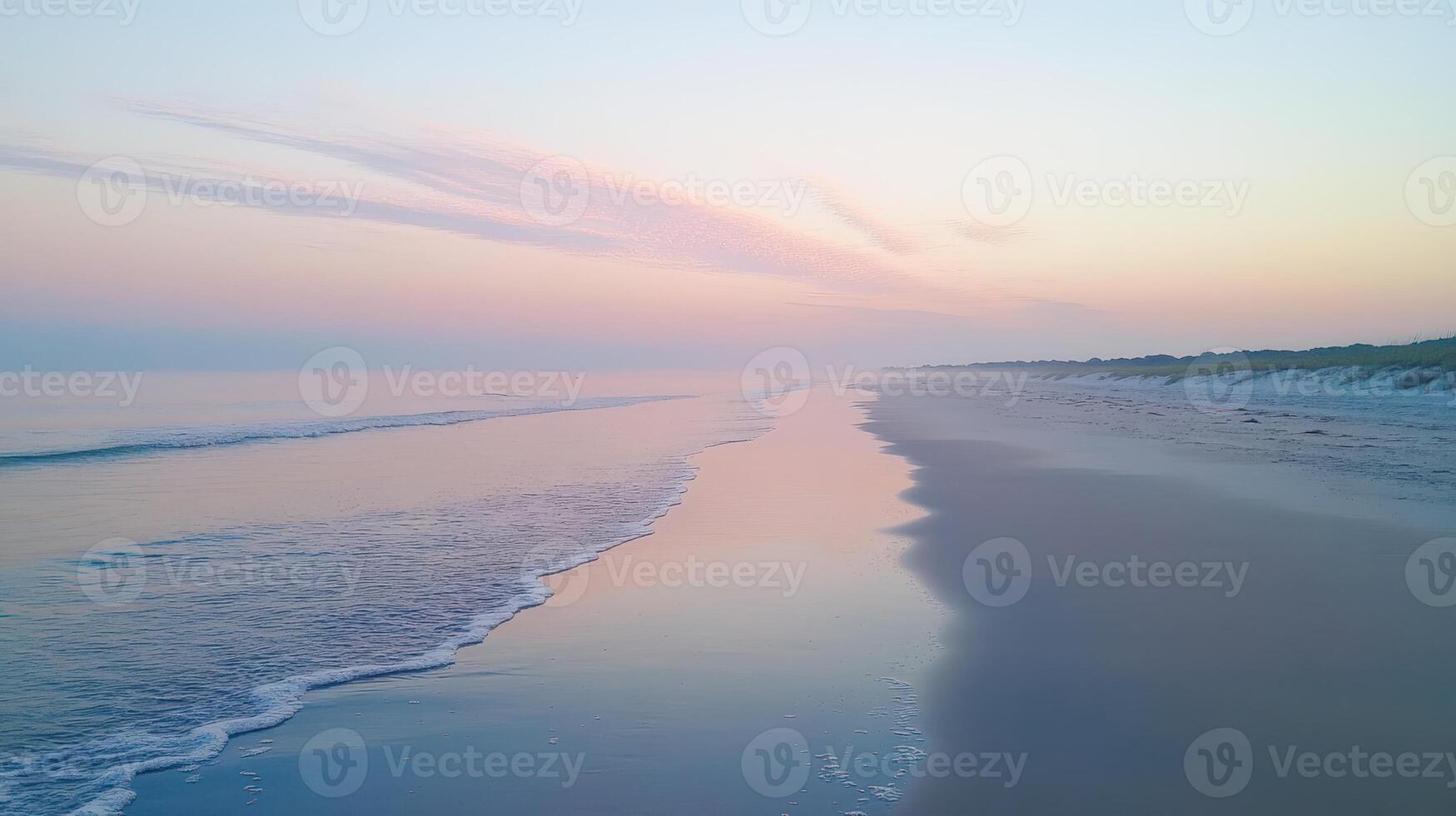 A serene beach at dawn with calm waves and soft pastel colors reflecting on the water photo