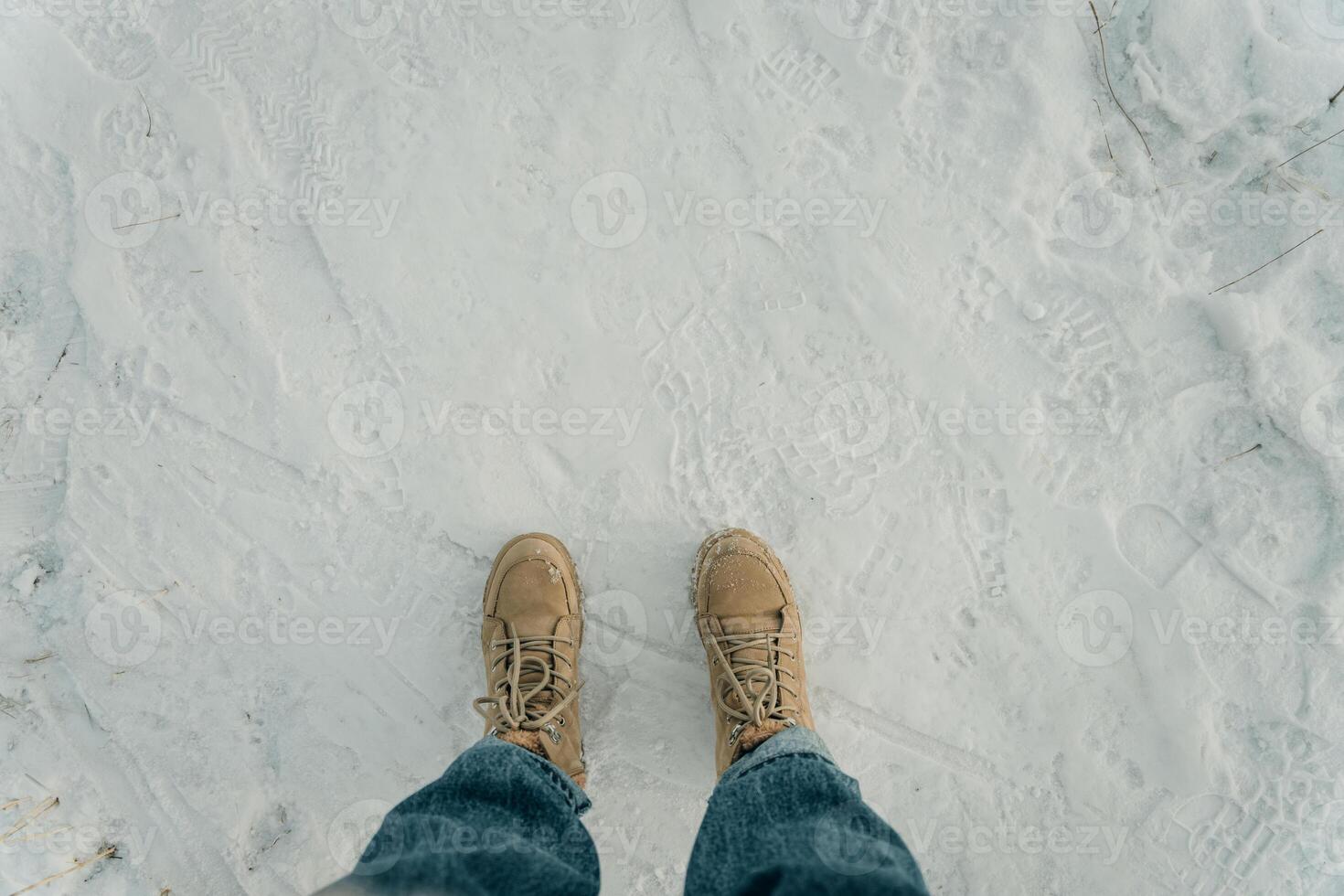 Feet in black trekking boots on snow. Winter walking. Top view photo
