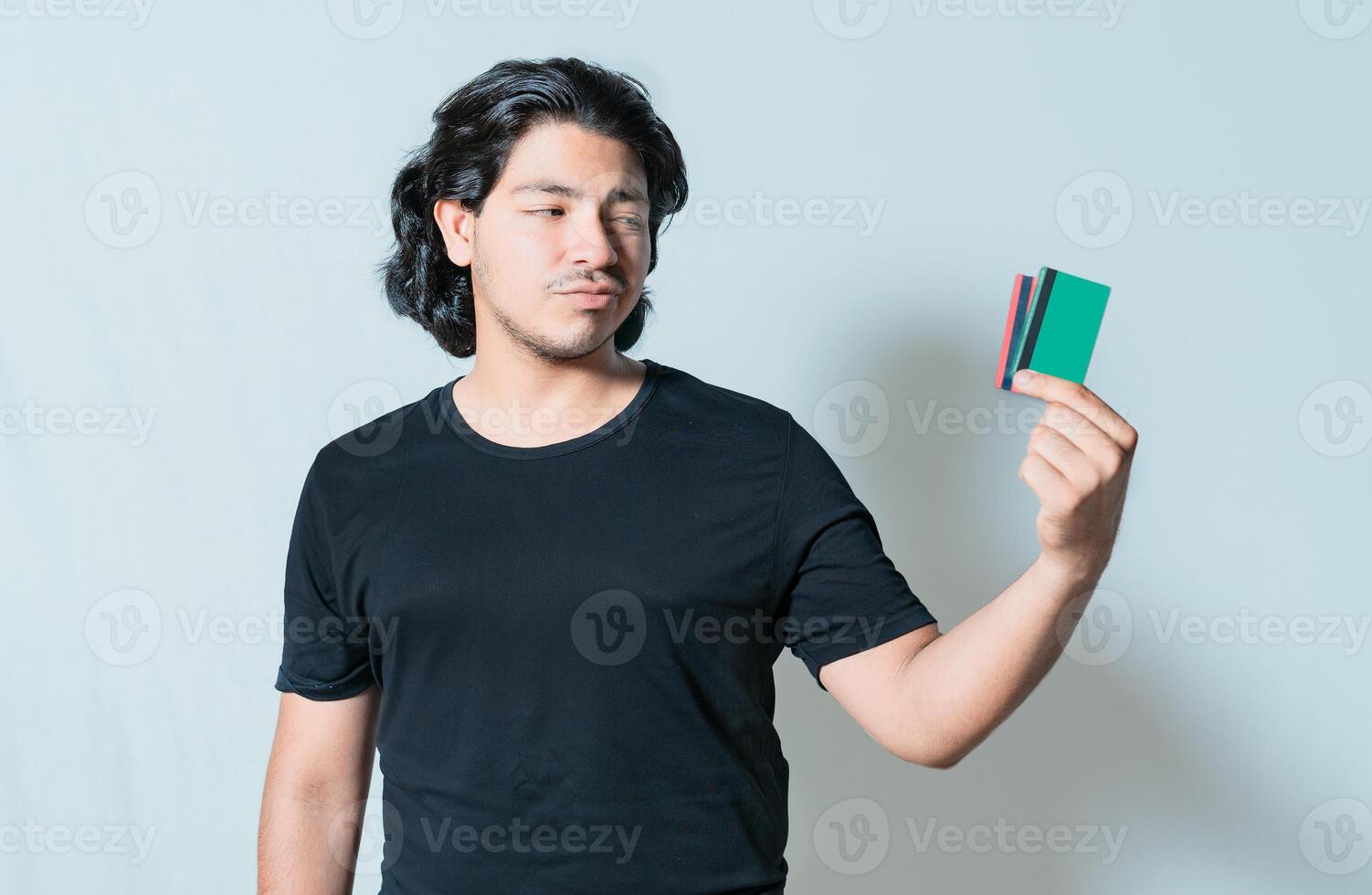 Unsure guy holding a credit card isolated. Confused man holding and looking at credit card photo