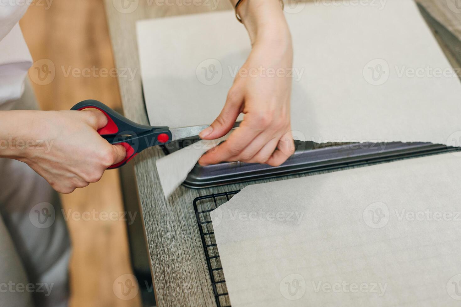 Hand holding up a sheet of baking paper and cut using a pair of scissors, photo