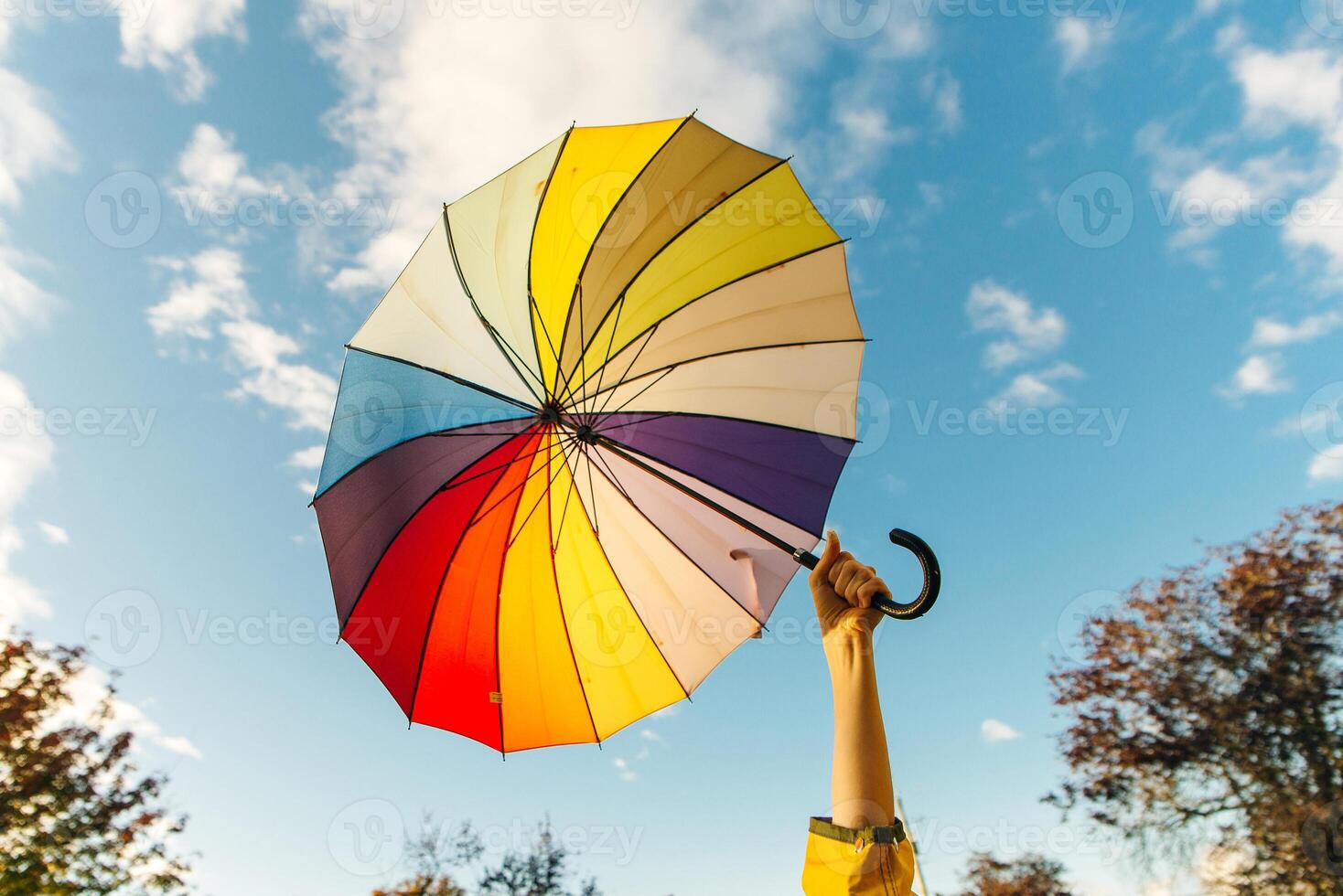 young woman standing with a multi-colored umbrella and rotates it against with a blue sky, photo