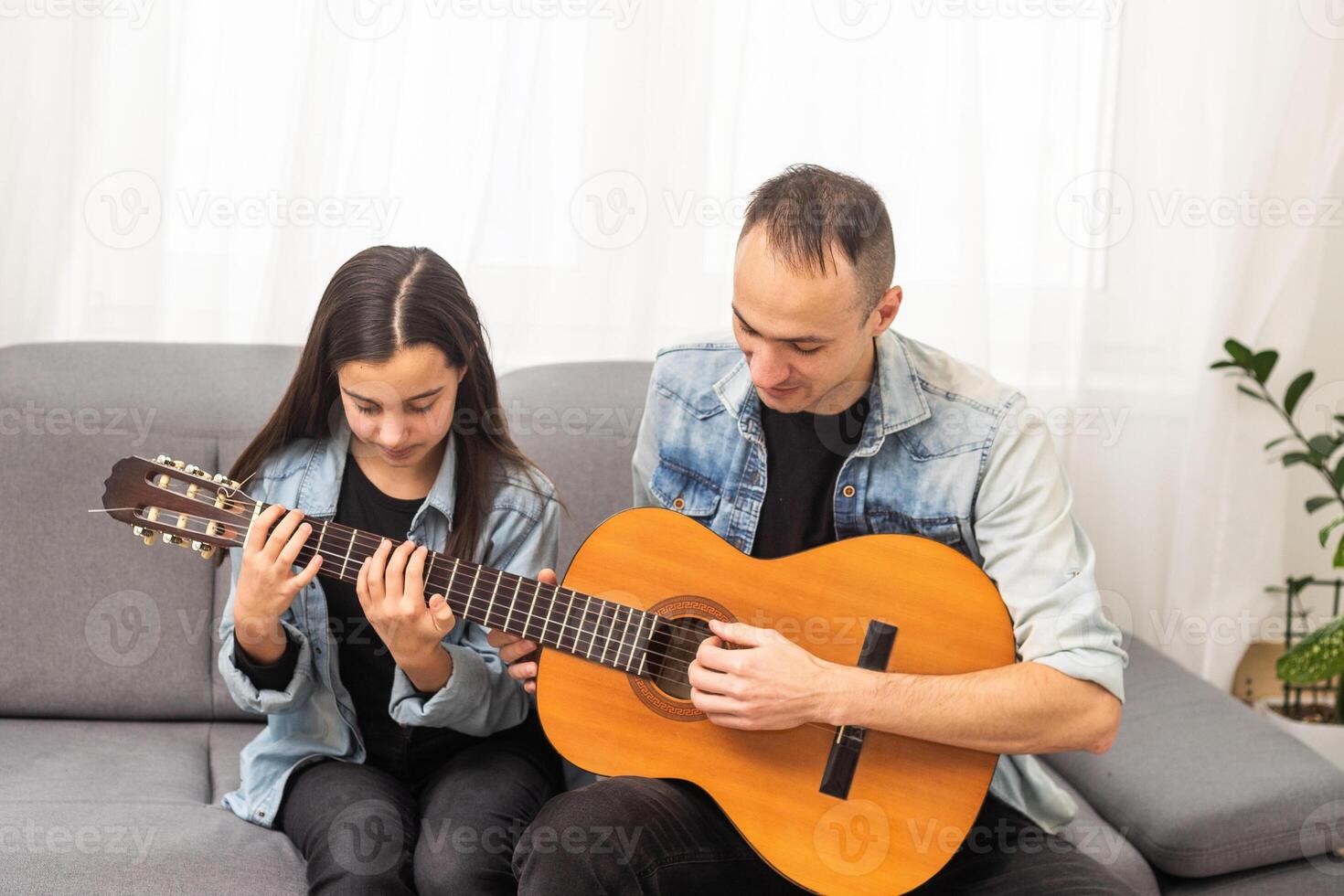 Father guy teaching girl teenager daughter guitar playing at home. Family musical lessons with strings instrument photo
