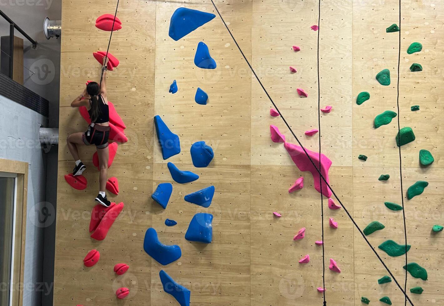 Teenage girl at indoor climbing wall. Kid having fun at bouldering wall. Child learning at climbing class. Sports healthy lifestyle. Youth at climbing summer camp photo