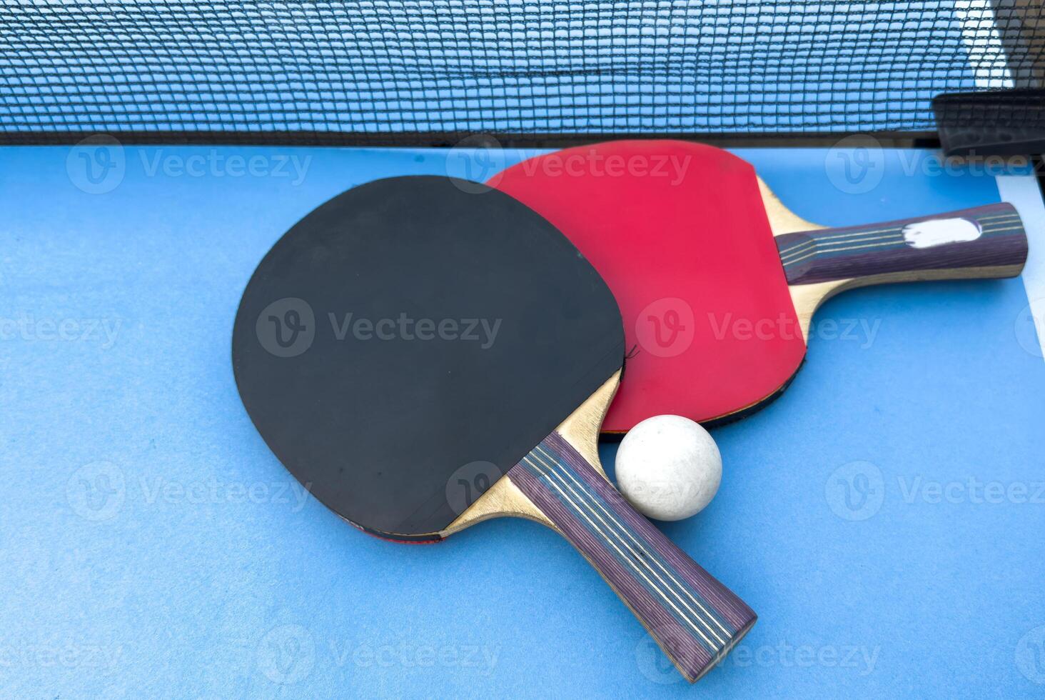 Red and black rackets for table tennis with white ball on blue background. Ping pong sports equipment in minimal style. Flat lay, top view, copy space photo