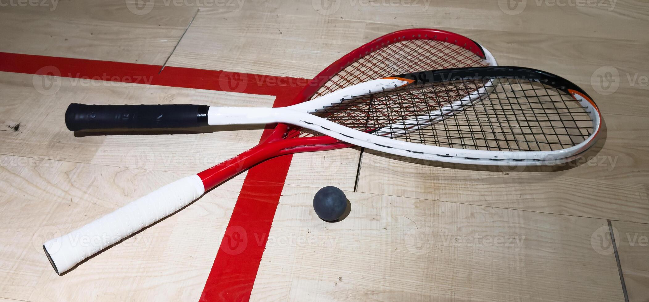 Two rackets and two squash balls lie on the parquet floor. Horizontal photo