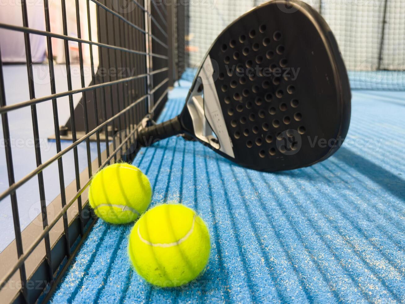 Padel racket and yellow ball behind net on a green court grass turf outdoors at sunset. Paddle is a racquet game. Professional sport concept with space for text photo