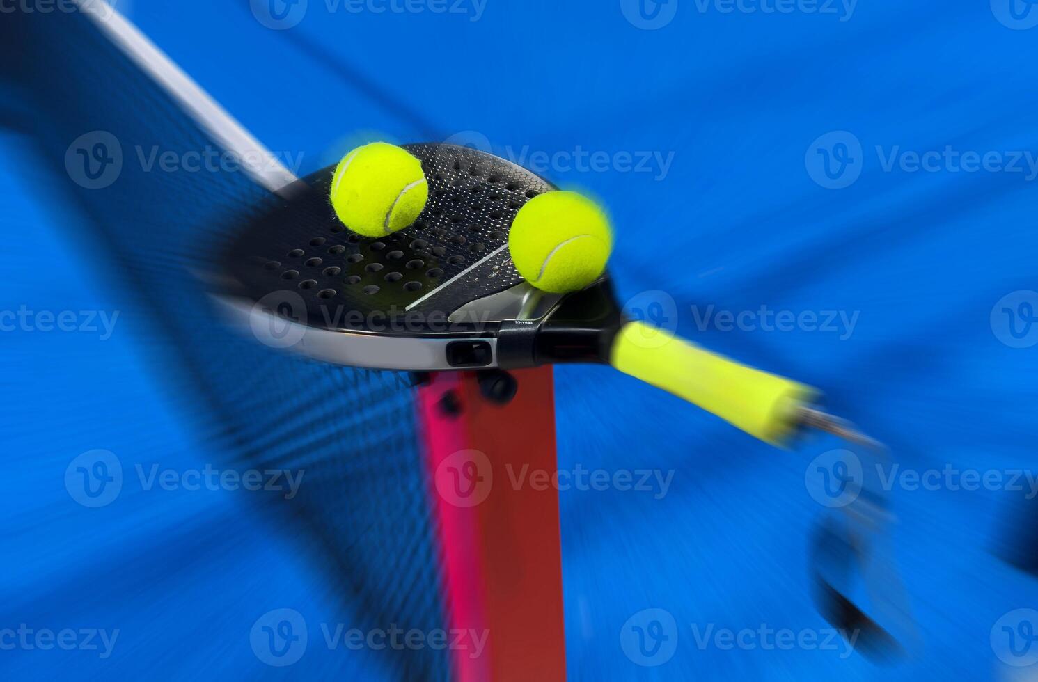 A padel or paddle tennis racket and a bright yellow tennis ball lie on a blue court. photo