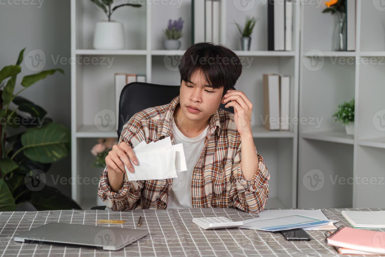 Stressed young man managing personal finances at home, reviewing bills and documents with a concerned expression. photo