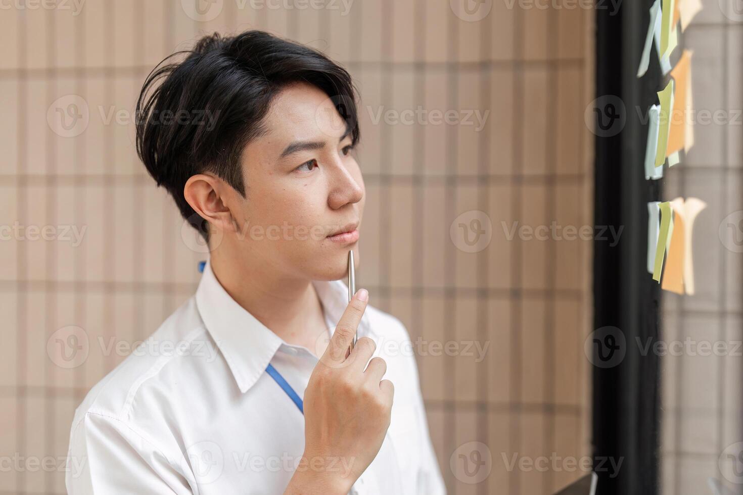 Young professional contemplating sticky notes on glass wall, strategizing tasks and improving workflow in modern office. photo