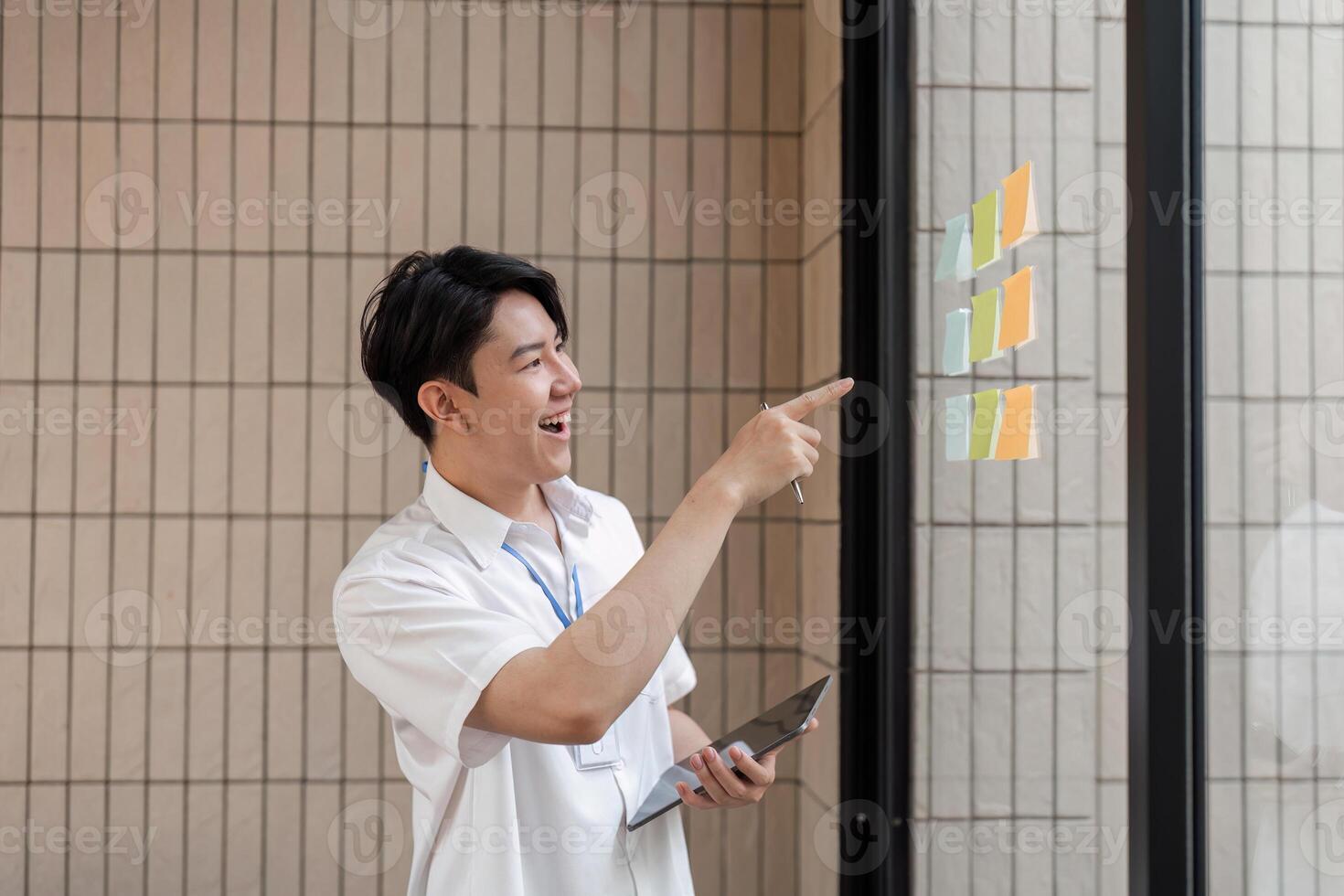 Young professional excitedly pointing at sticky notes on glass wall, discussing ideas and enhancing workflow in modern office. photo