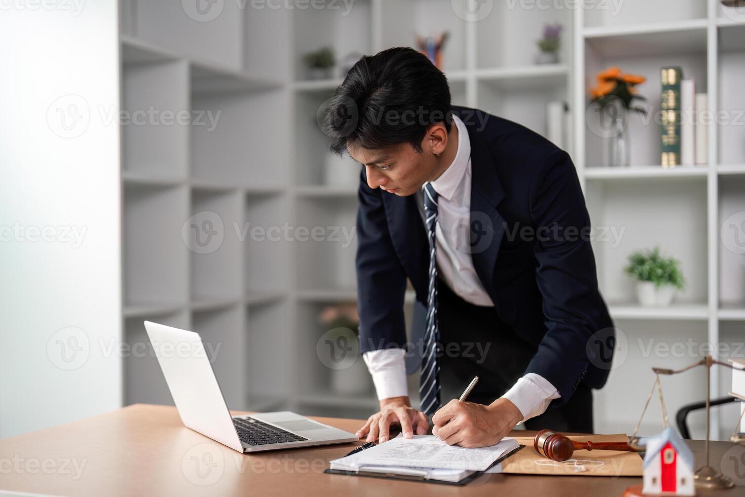 Young businessman writing notes and reviewing documents while standing in a modern office environment. photo
