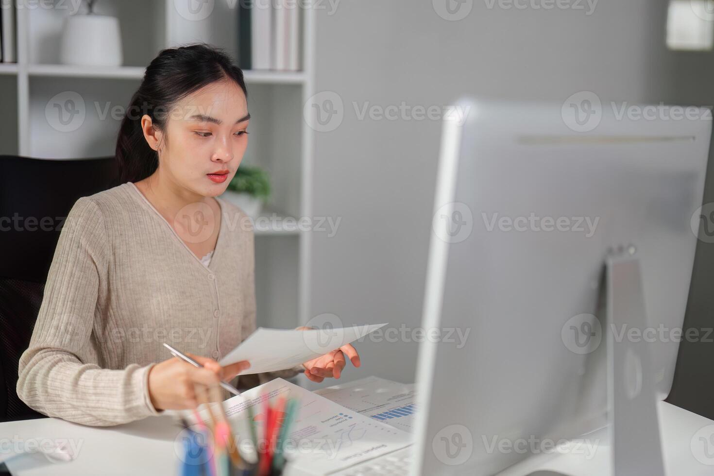 Focused office worker analyzing documents and taking notes at her desk. photo
