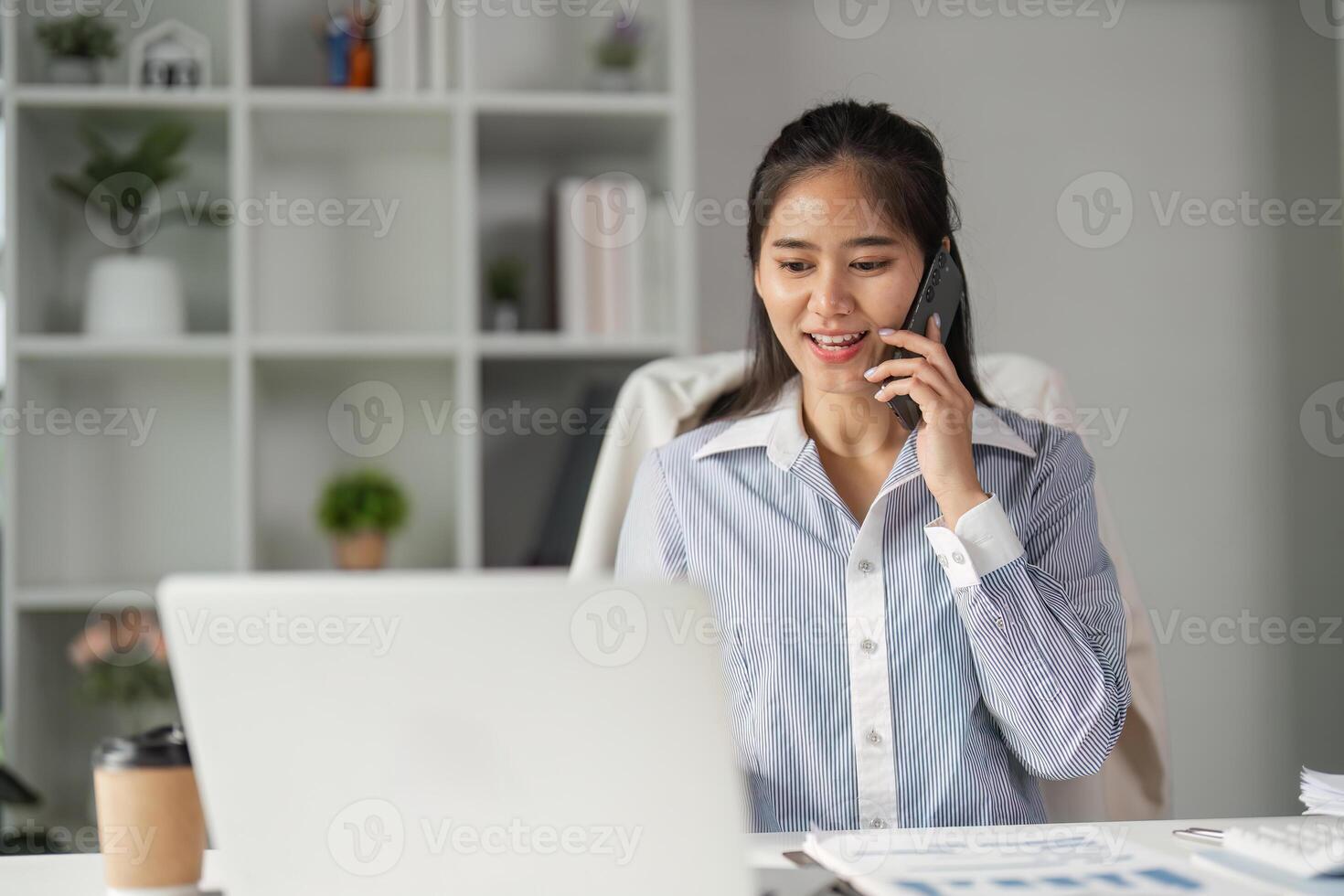 Finance professional happily engaging in a phone conversation while working at her desk. photo